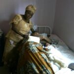 A Richard Akinnola Foundation Female representative handling over some cash to woman in a sick bed